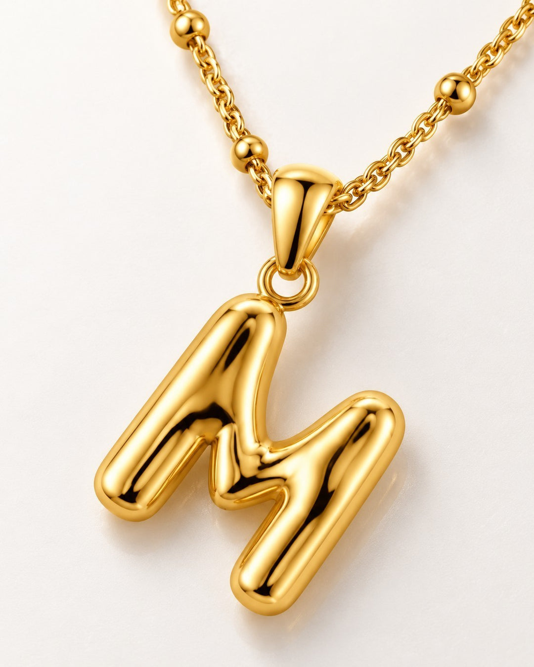 Elli Jewellery gold-toned chunky letter M pendant necklace on a delicate beaded chain against a white background.