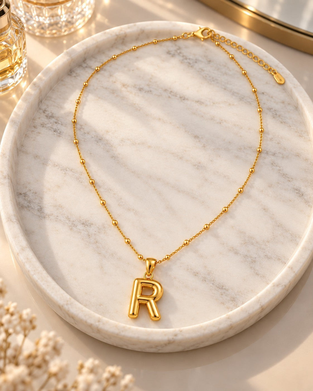 Elli Jewellery gold plated chunky letter R initial pendant necklace on a marble tray with a delicate beaded chain.