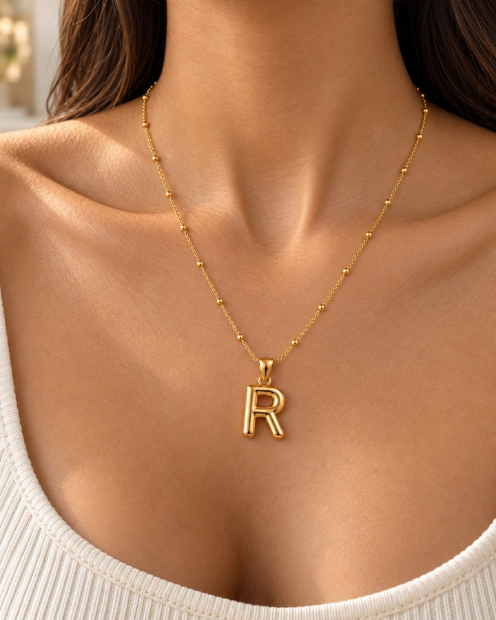 Elli Jewellery chunky gold plated letter R initial pendant necklace worn on a delicate beaded chain by a woman.