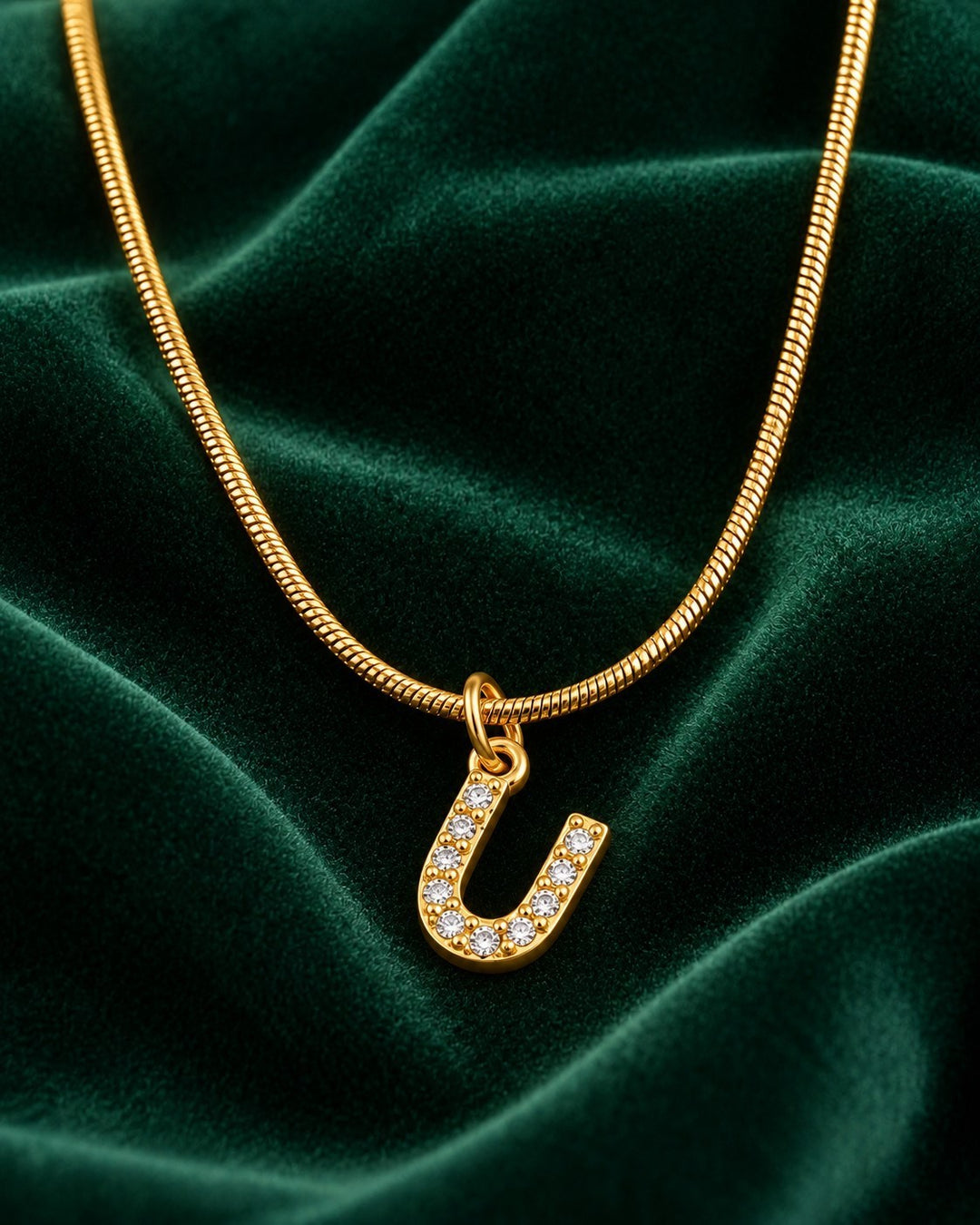 Elli Jewellery gold plated letter U initial pendant necklace with sparkling crystals on a green velvet background