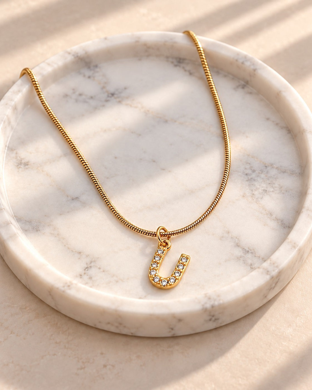 Elli Jewellery gold plated letter U initial pendant necklace with sparkling stones on a marble tray