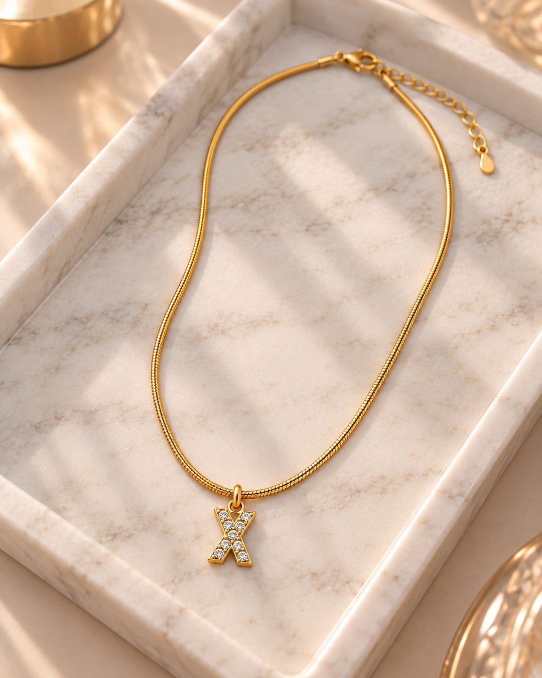 Elli Jewellery gold plated waterproof letter X initial pendant necklace with sparkling stones on a marble tray