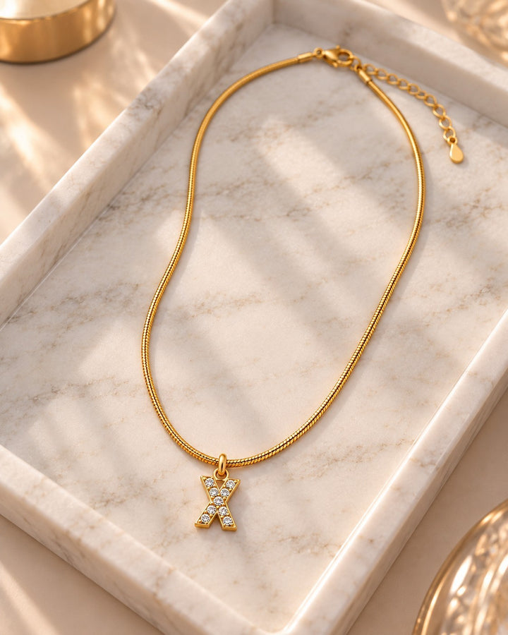 Elli Jewellery gold plated waterproof letter X initial pendant necklace with sparkling stones on a marble tray