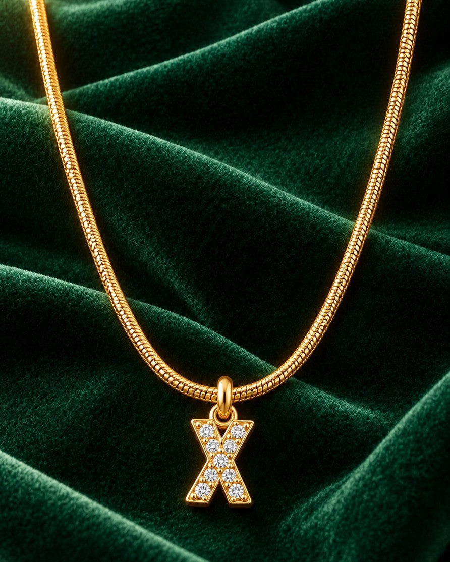 Elli Jewellery gold plated letter X initial pendant necklace with sparkling stones on a green velvet background