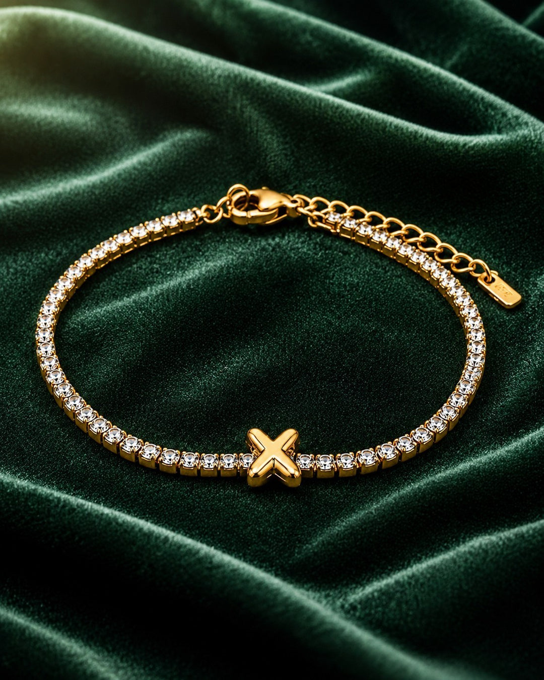 Elli Jewellery gold-plated tennis bracelet featuring a central letter X charm and sparkling crystals on green velvet.