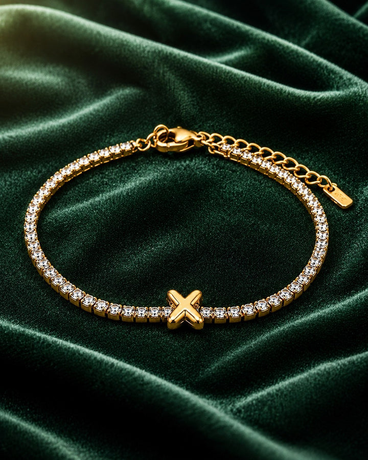 Elli Jewellery gold-plated tennis bracelet featuring a central letter X charm and sparkling crystals on green velvet.