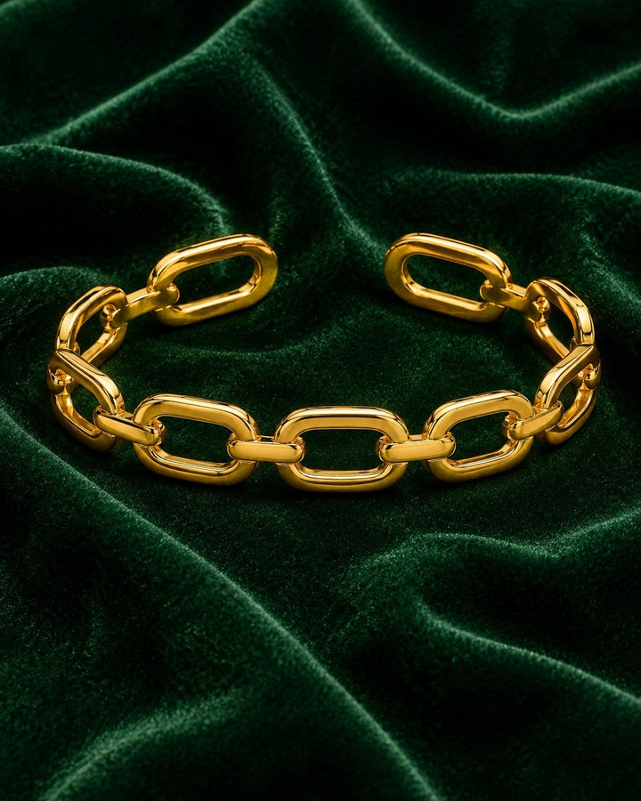 Elli Jewellery gold plated chunky link chain cuff bangle resting on a luxurious dark green velvet fabric background.