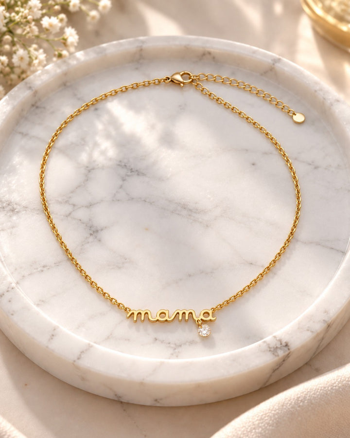 Elli Jewellery gold plated dainty MAMA script pendant necklace with a small crystal charm on a marble tray.