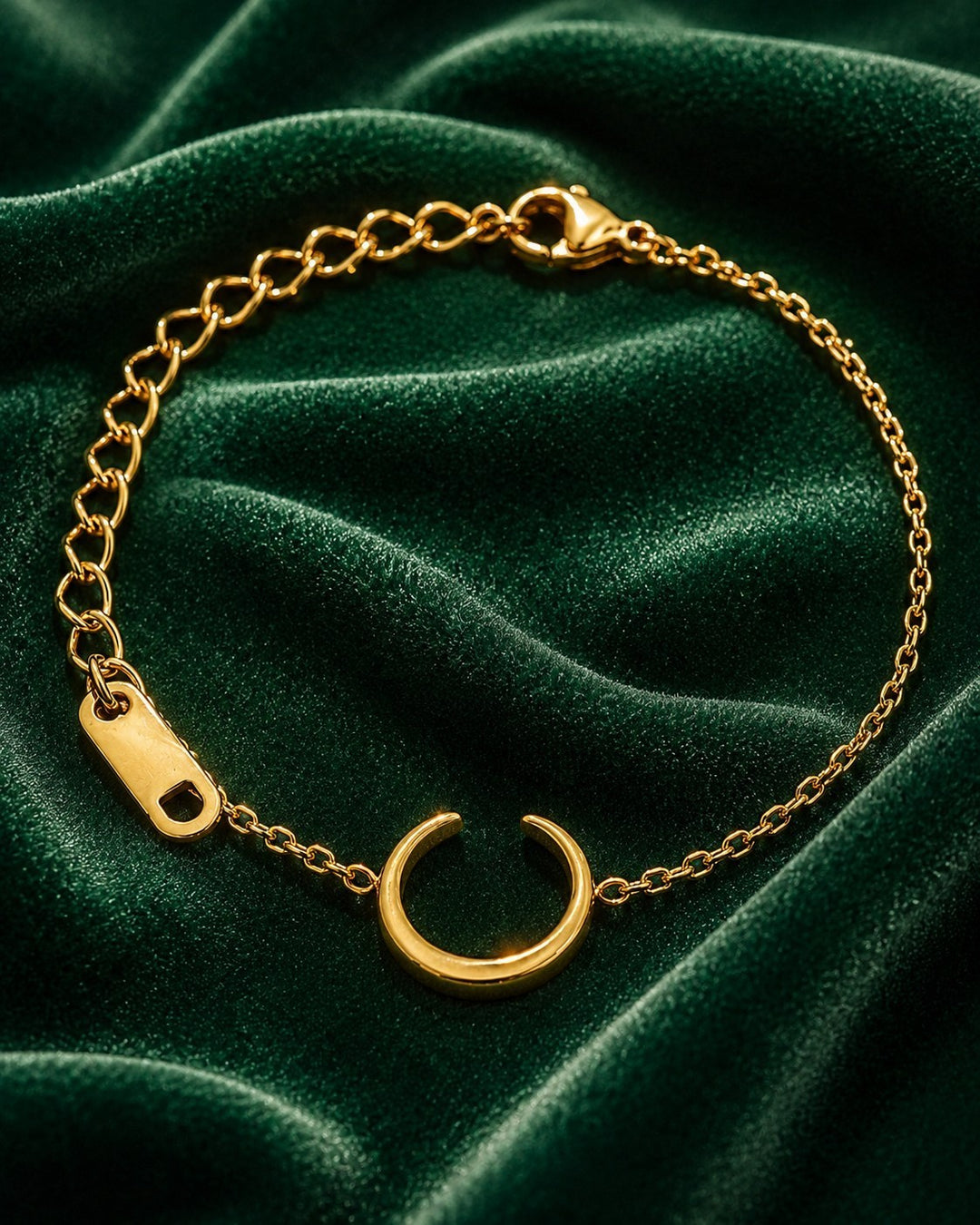 Elli Jewellery gold plated minimalist chain bracelet with a crescent charm on a dark green velvet background