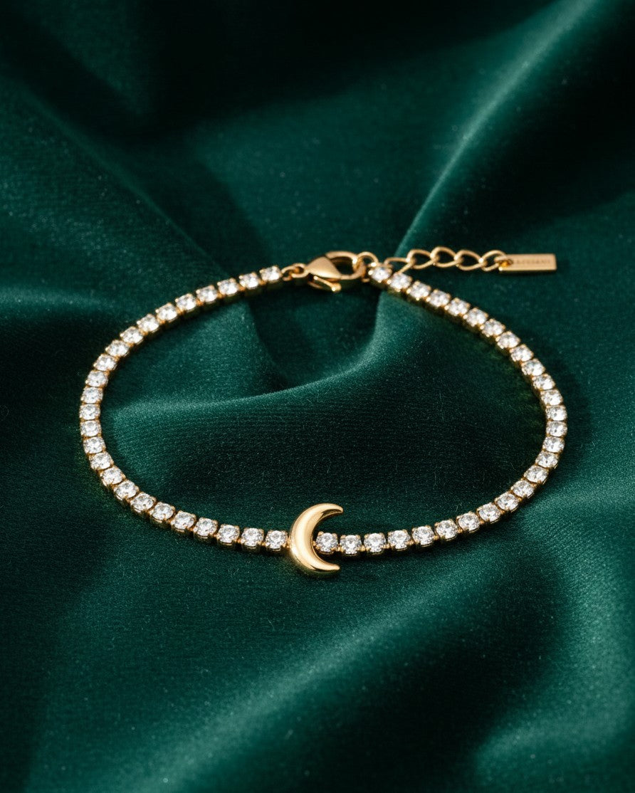Elli Jewellery gold plated crescent moon charm bracelet with sparkling crystals on a dark green velvet background.