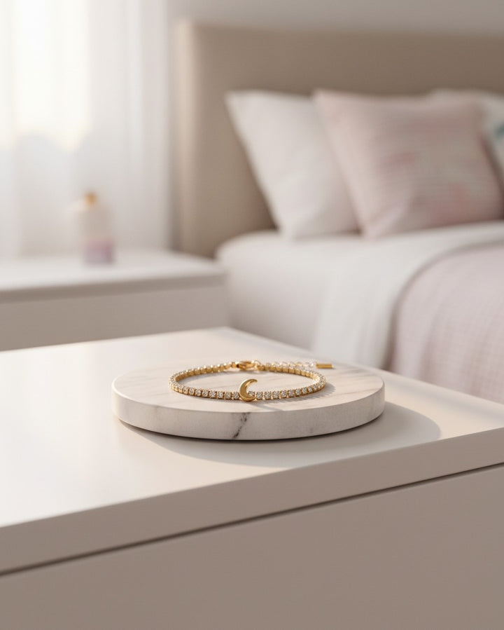 Elli Jewellery gold plated tennis bracelet with a crescent moon charm resting on a marble display stand in a bedroom.