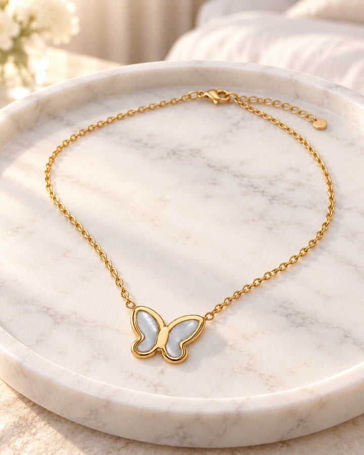 Elli Jewellery gold plated butterfly pendant necklace with iridescent mother of pearl inlay on a marble tray.