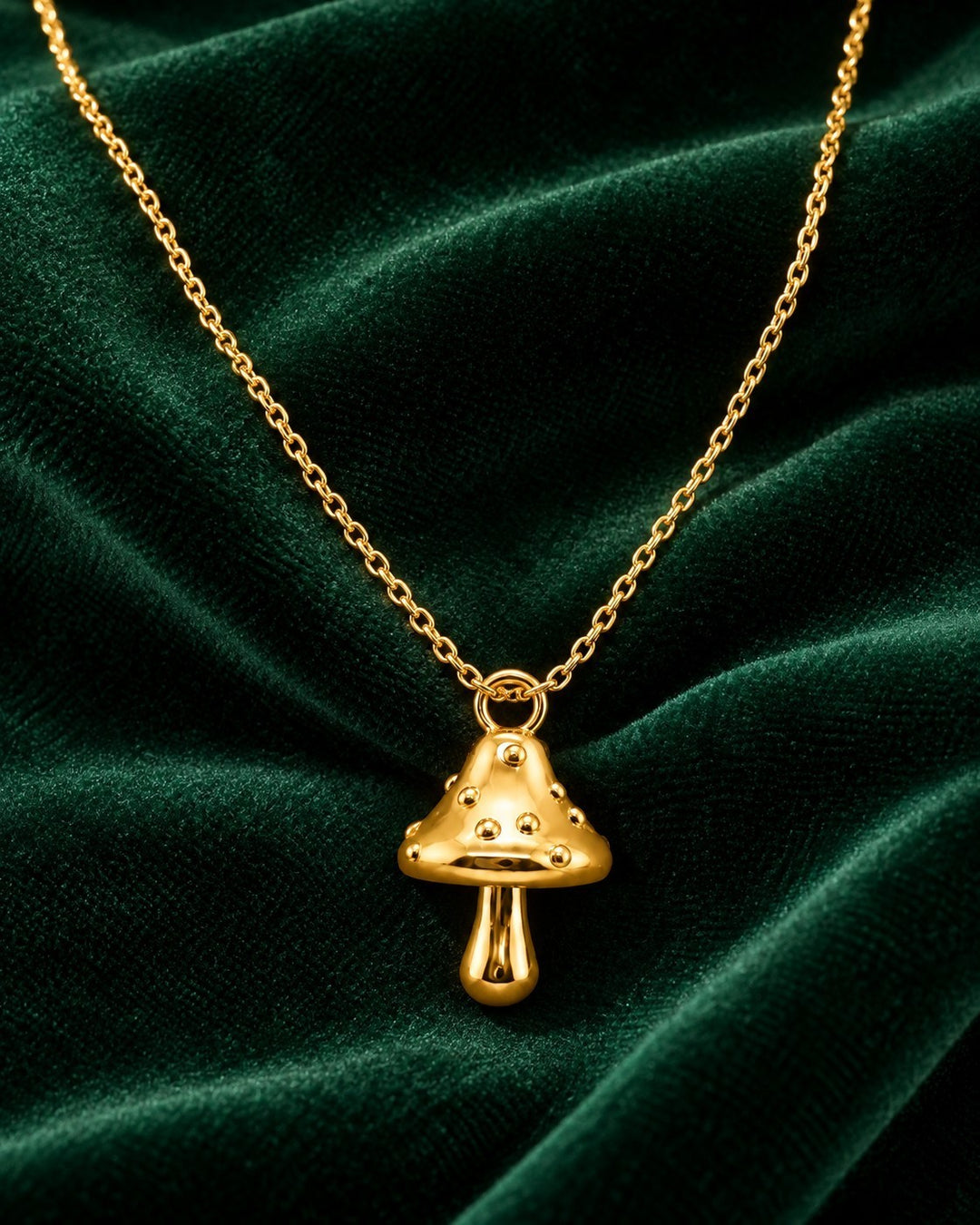 Elli Jewellery gold plated mushroom charm pendant necklace on a dark green velvet background