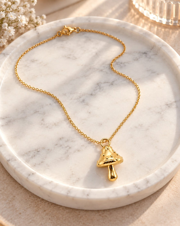 Elli Jewellery gold plated mushroom charm pendant necklace on a white marble tray with delicate white flowers.