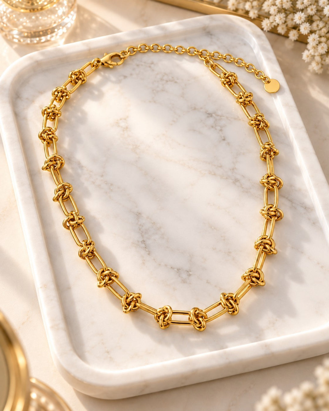 Elli Jewellery gold plated waterproof oval link chain necklace with chunky interlocking knots on a marble tray