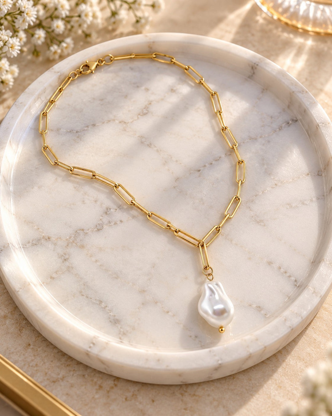 Elli Jewellery gold plated paperclip chain necklace featuring a lustrous baroque faux pearl pendant on a marble tray.