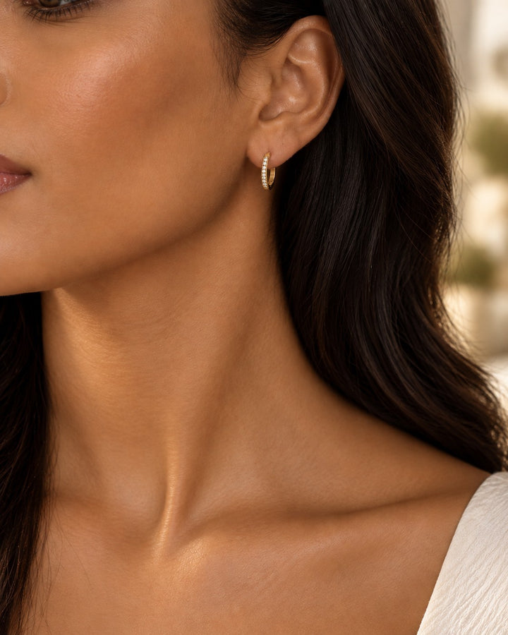 Elli Jewellery gold plated hoop earrings with clear pavé crystals worn by a woman with dark hair