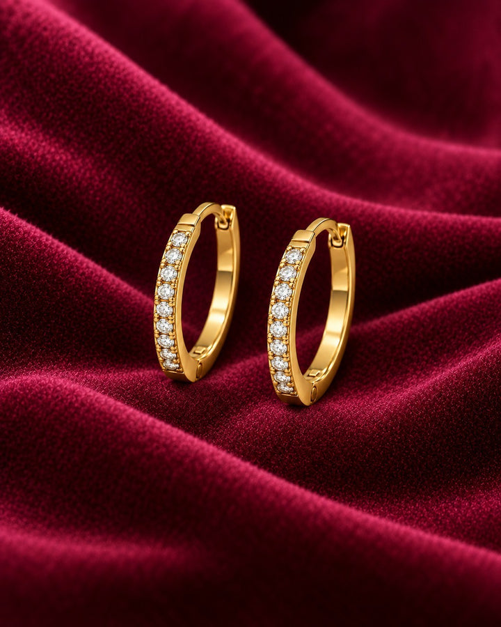 Elli Jewellery gold plated hoop earrings with pavé-set clear crystals on a rich burgundy velvet background.