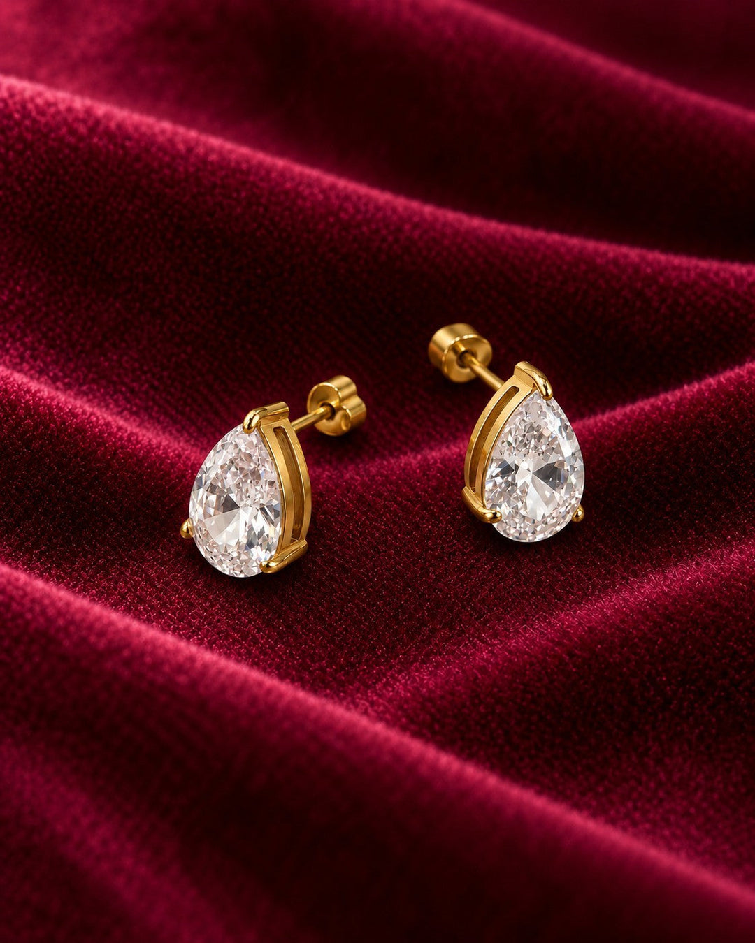 Elli Jewellery pear shaped cubic zirconia stud earrings with a gold plated finish resting on deep red velvet fabric.