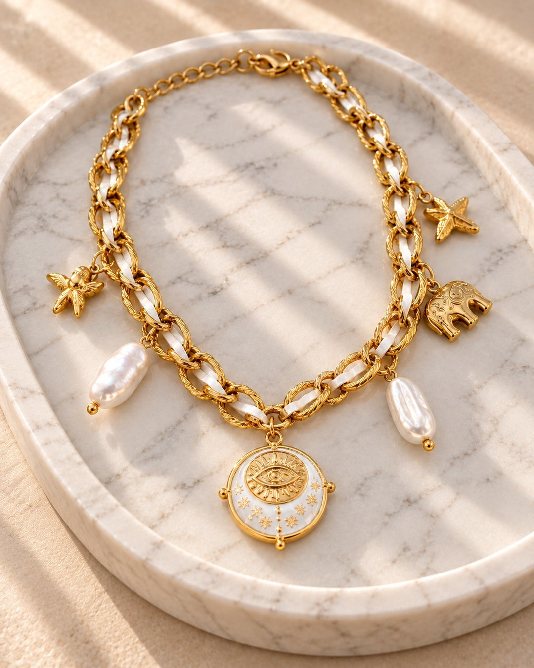 Elli Jewellery gold plated chain necklace featuring baroque pearl, starfish, and elephant charms on a marble tray.