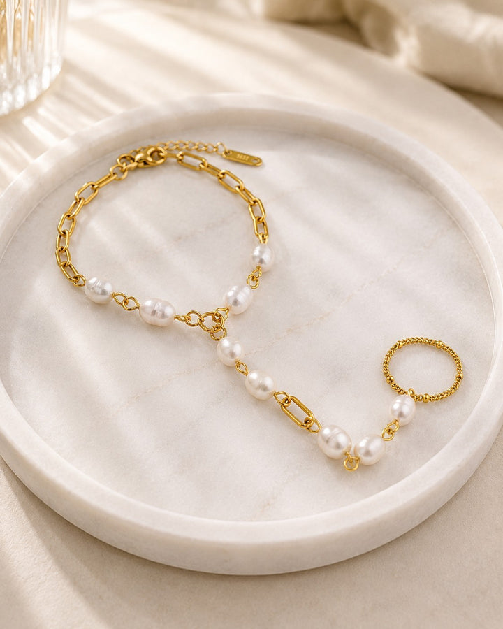 Elli Jewellery gold plated hand chain bracelet featuring lustrous pearls and a delicate ring on a marble tray