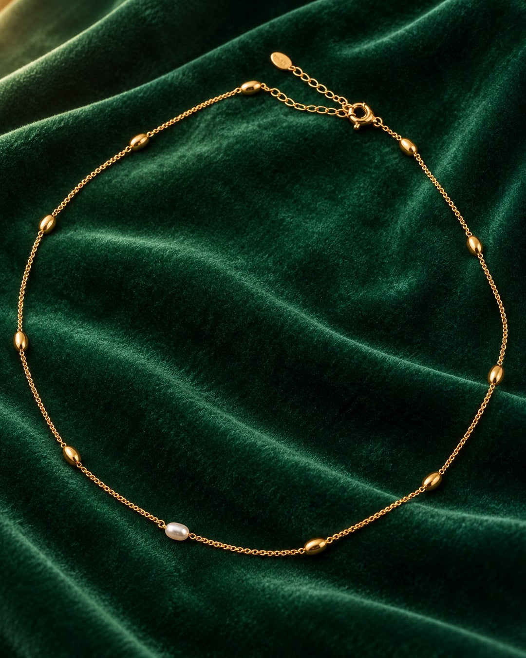 Elli Jewellery gold plated chain necklace with delicate freshwater pearl beads on a dark green velvet background