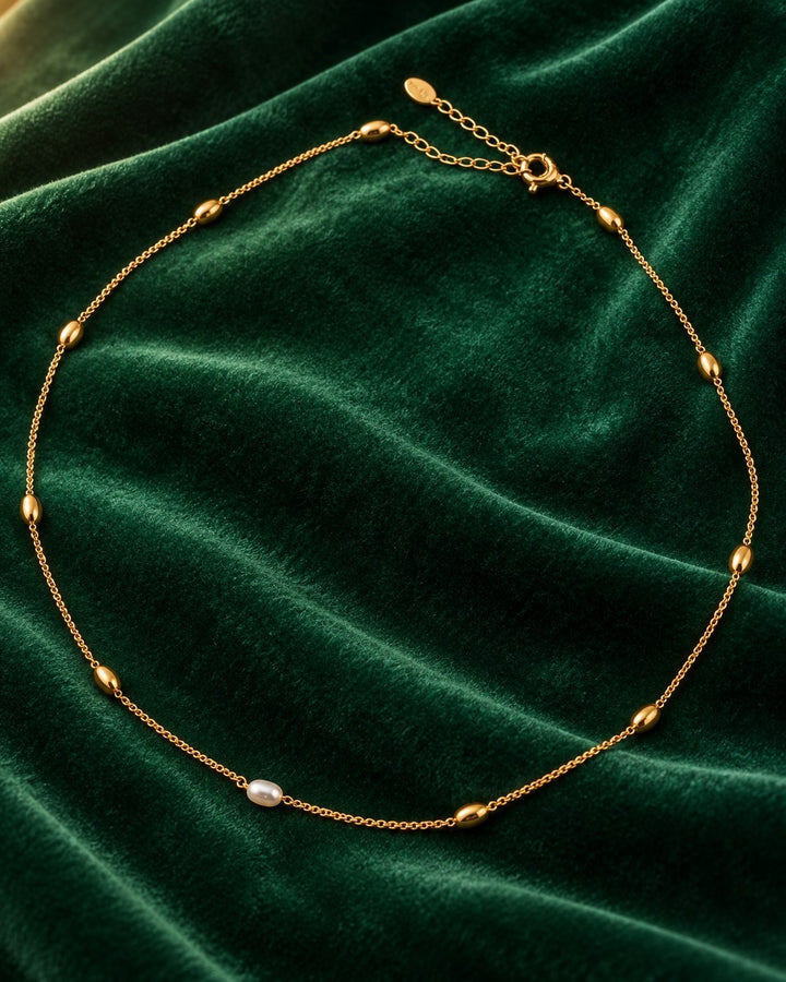 Elli Jewellery gold plated chain necklace with delicate freshwater pearl beads on a dark green velvet background