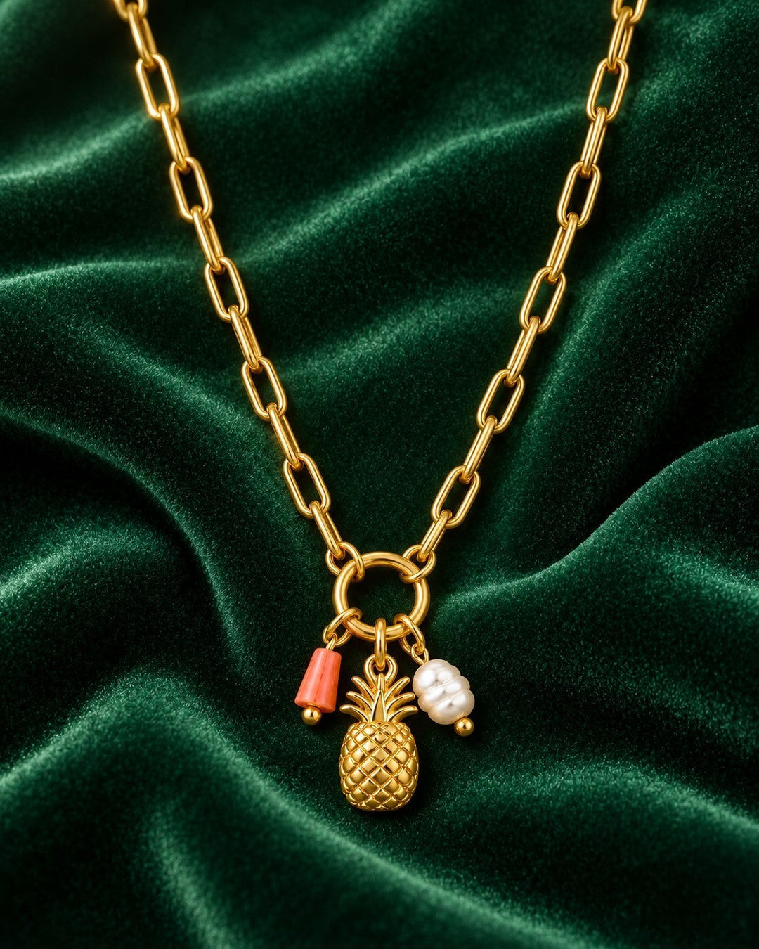 Elli Jewellery gold plated pineapple pendant necklace with coral and pearl charms on a green velvet background