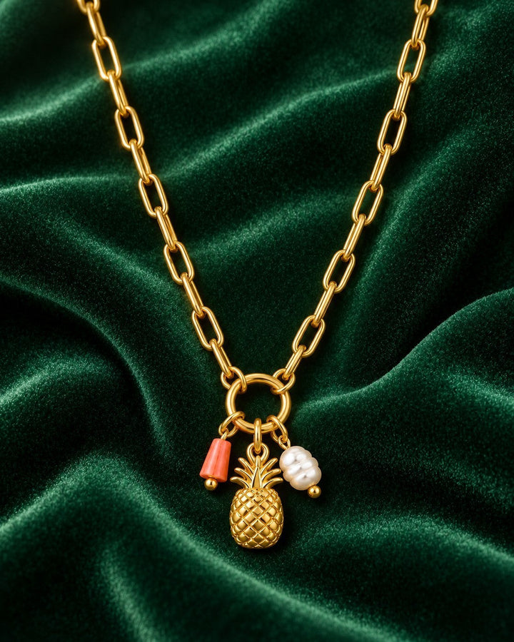 Elli Jewellery gold plated pineapple pendant necklace with coral and pearl charms on a green velvet background