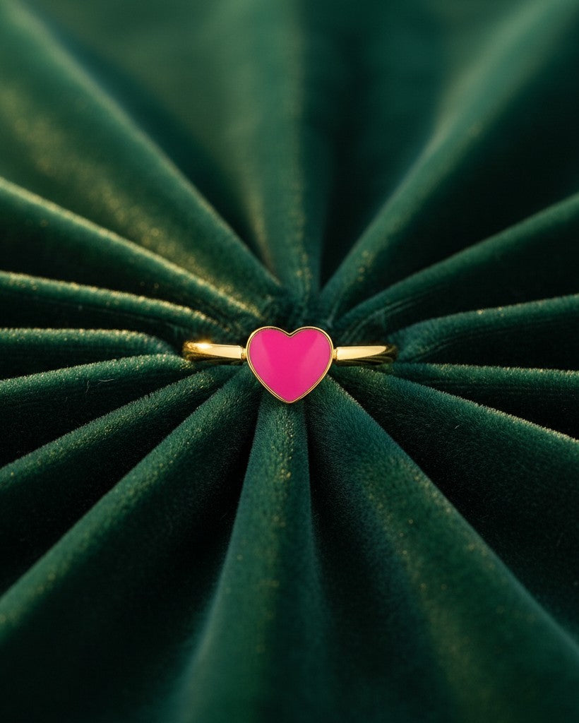 Elli Jewellery gold plated ring featuring a vibrant pink enamel heart, displayed on a dark green velvet background.