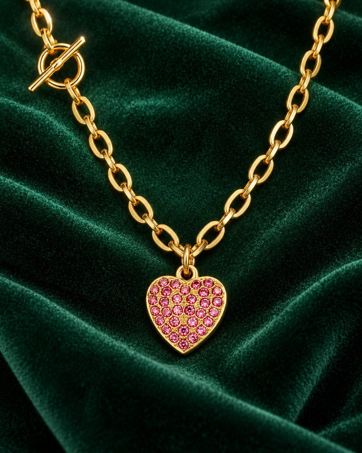 Elli Jewellery gold plated necklace featuring a pink diamante heart pendant and T-bar clasp on green velvet fabric.
