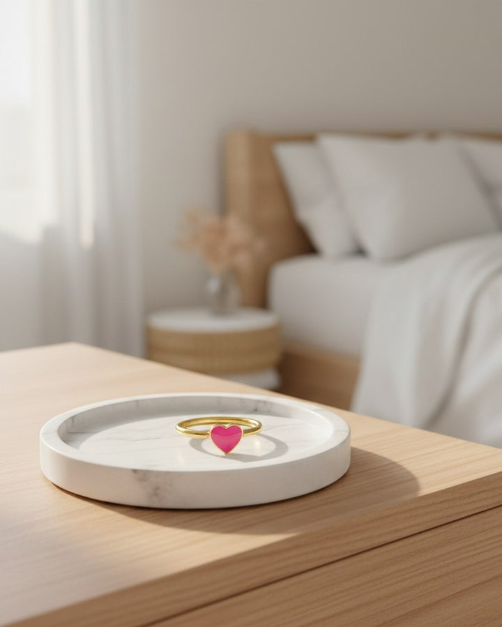 Elli Jewellery gold plated ring featuring a vibrant pink enamel heart, displayed on a white marble tray.