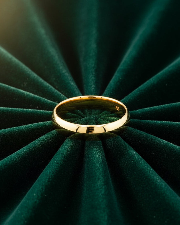 Elli Jewellery gold plated slim bangle bracelet resting on a dark green pleated velvet background