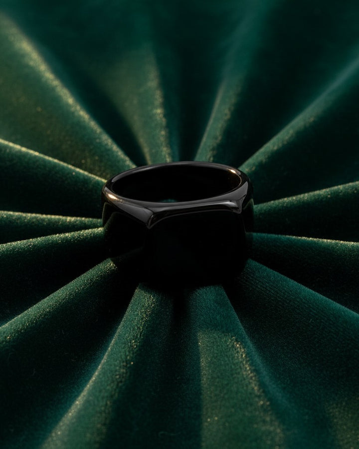 Elli Jewellery gold plated signet ring with a smooth black enamel face displayed on a pleated dark green fabric