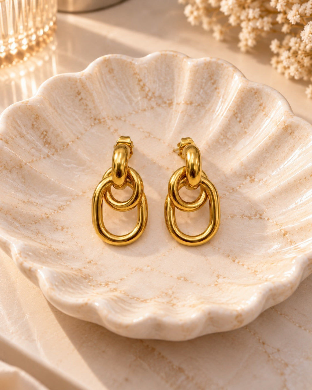 Elli Jewellery gold plated waterproof drop earrings with interlocking oval links resting in a decorative shell dish