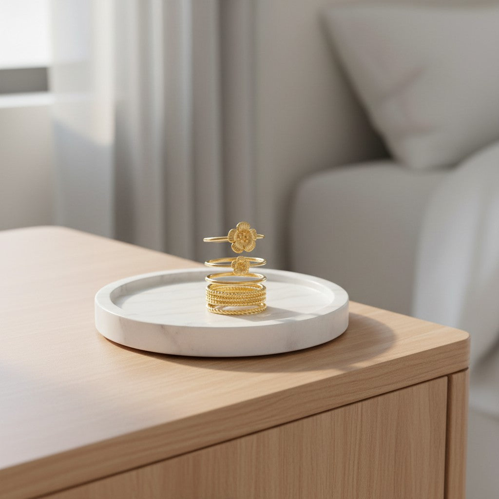Elli Jewellery 3 piece gold plated flower ring set displayed on a white marble tray on a wooden bedside table.