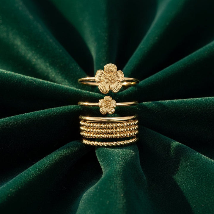 Elli Jewellery 3 piece gold plated flower ring set featuring textured floral designs on a dark green velvet background