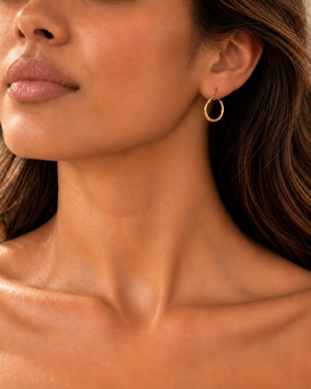 Elli Jewellery classic polished gold plated hoop earrings worn by a woman with long wavy hair