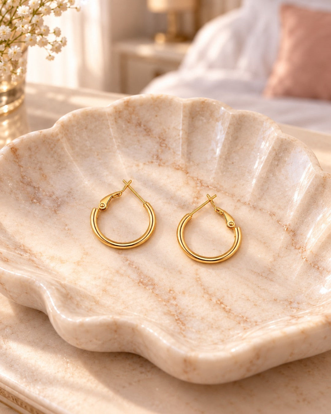 Elli Jewellery polished 18ct gold plated hoop earrings with a hinged clasp resting in a decorative shell dish.