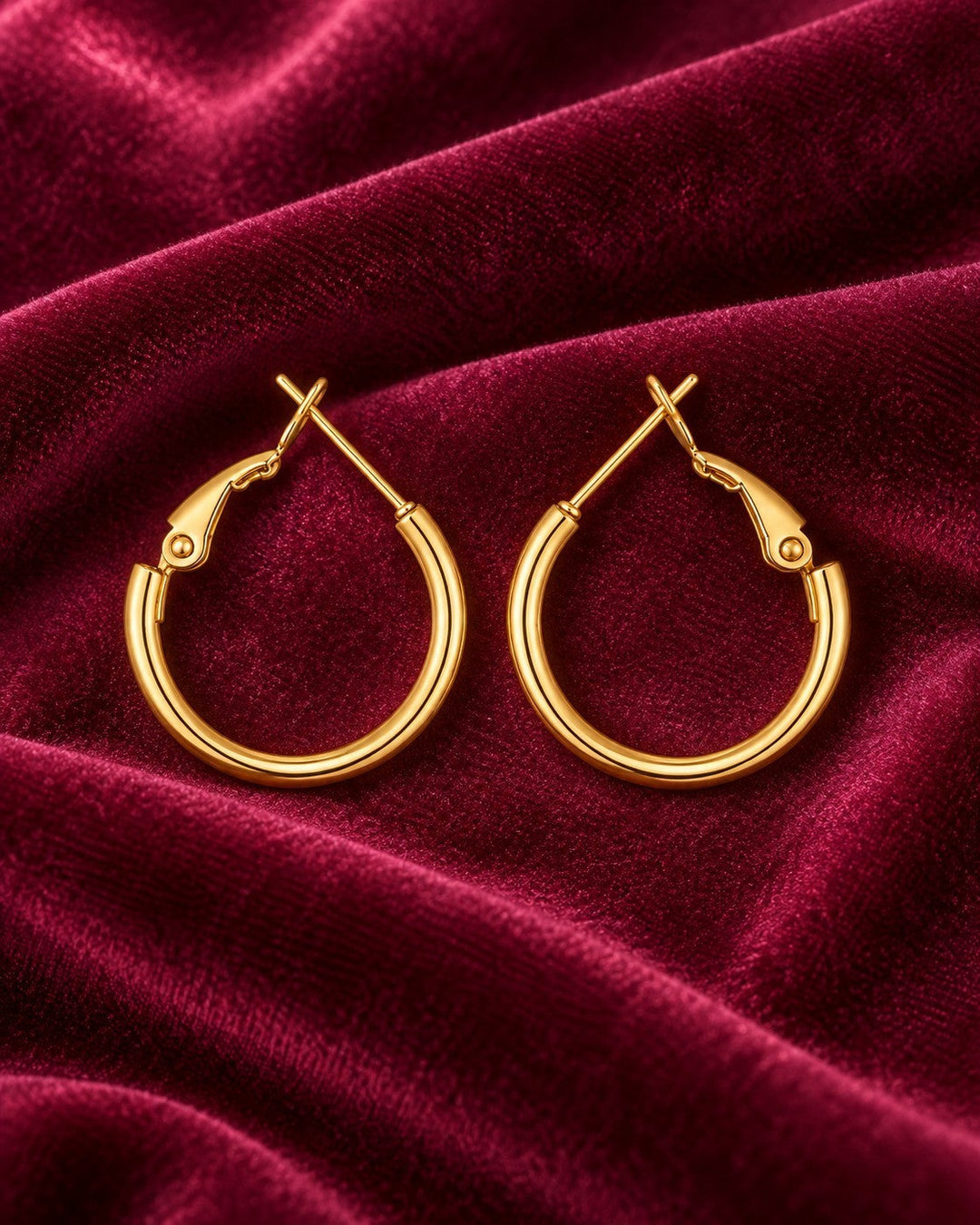 Elli Jewellery polished 18ct gold plated hoop earrings with a hinged clasp resting on deep red velvet fabric.