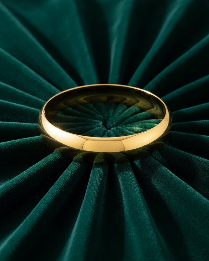 Elli Jewellery gold plated waterproof slim bangle resting on a dark green pleated velvet background.