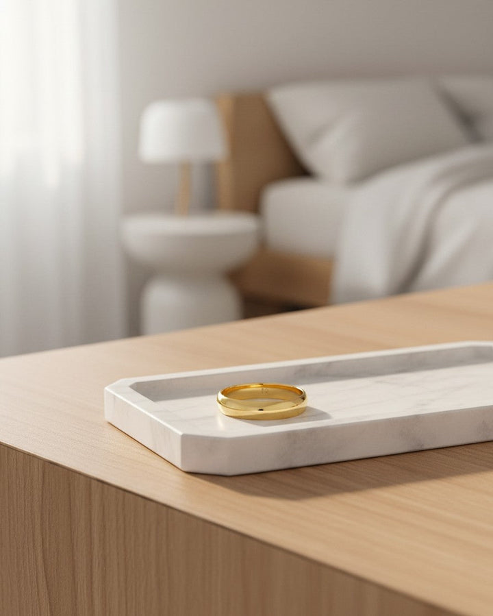 Elli Jewellery gold plated slim 1cm waterproof bangle bracelet resting on a white marble tray in a bedroom setting