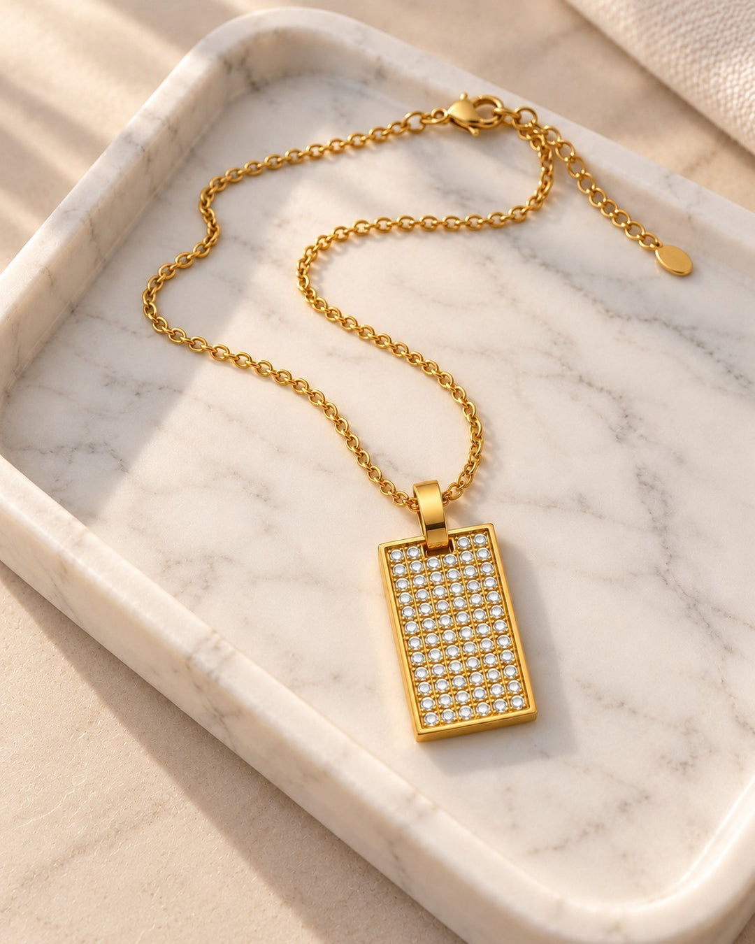 Elli Jewellery gold plated rectangle pendant necklace with a crystal inlay on a marble tray.