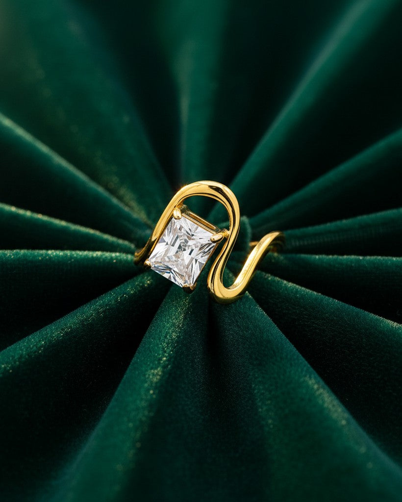 Elli Jewellery gold plated ring featuring a geometric rectangular clear stone on a smooth, curved band on green velvet.