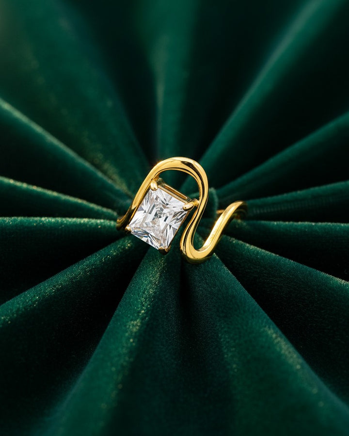Elli Jewellery gold plated ring featuring a geometric rectangular clear stone on a smooth, curved band on green velvet.