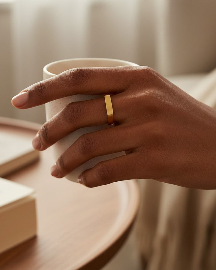 Elli Jewellery gold plated rectangular signet ring worn on a finger while holding a ceramic cup