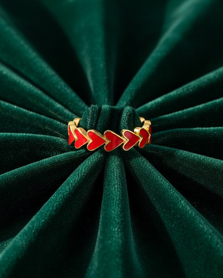 Elli Jewellery gold plated ring featuring a cluster of vibrant red enamel hearts on a dark green velvet background.