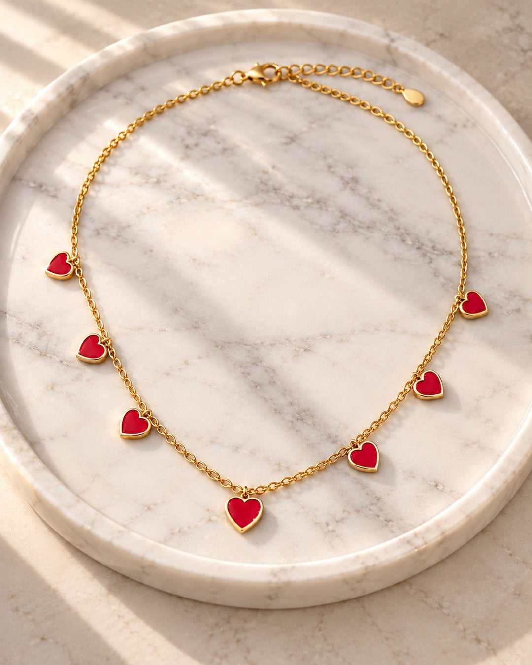 Elli Jewellery gold plated necklace featuring multiple small ruby red crystal heart charms on a delicate chain.