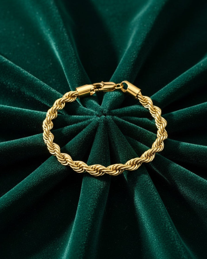 Elli Jewellery gold plated rope chain bracelet resting on a dark green velvet background