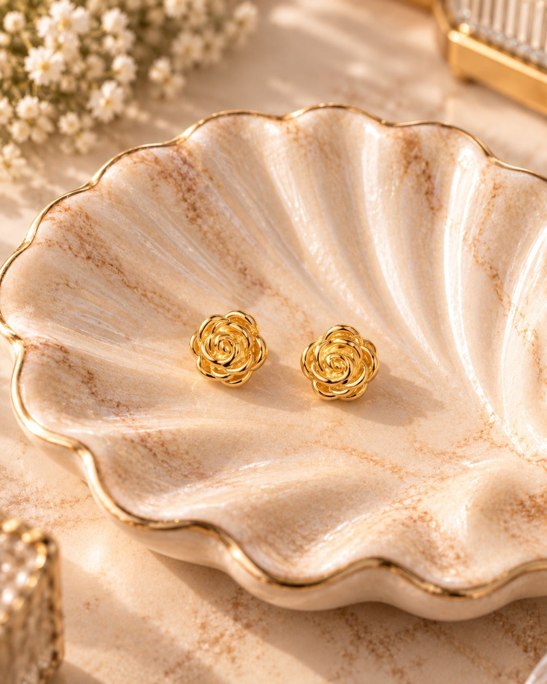 Elli Jewellery gold plated rosette stud earrings with sculptural flower petals resting on a decorative shell dish.